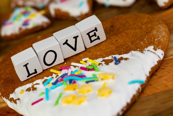 Состав глазурованного имбирного хлеба в форме сердец и слова "Любовь", расположенного на деревянной доске - Фото, изображение
