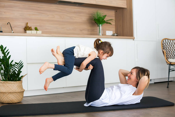 Woman and her cute little daughter are doing some exercises together at home - Fotografie, Obrázek