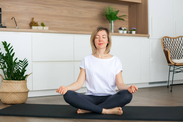 Relaxing woman sitting in a lotus position while doing yoga at home - Photo, Image