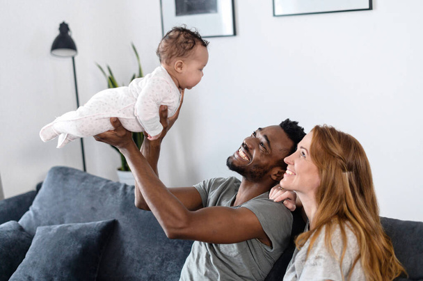 Multiracial family with baby girl sit on the couch - Foto, Imagen