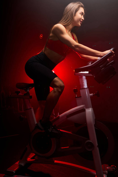 positive brunette woman cyclist. she is exercising at gym - Foto, afbeelding