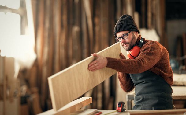 brutal man carpenter in knitted hat   working in a workshop - Photo, Image