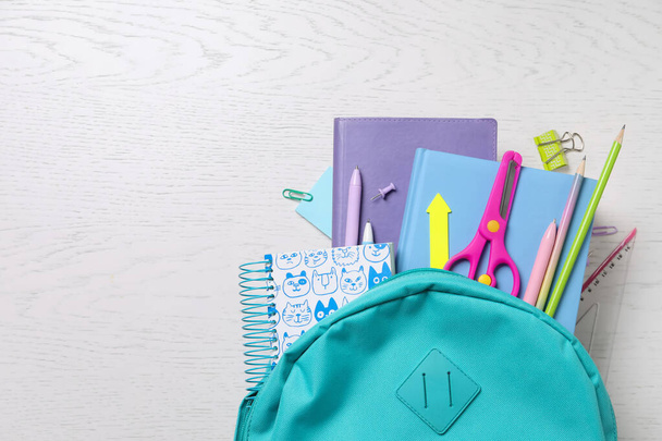 Schoolbag with books and stationery on wooden table, flat lay. Space for text - 写真・画像