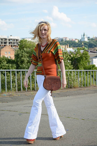 Beyaz pantalonlu moda düşkünü ve yürüyüşünde güzel bir retro çanta. - Fotoğraf, Görsel