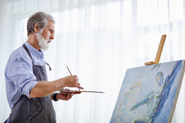 mature grey haired artist man painting using painter palette - 写真・画像