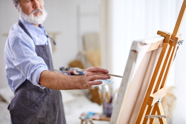 gray bearded artist painting on easel, canvas - Foto, Imagen