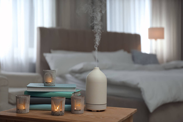 Aroma oil diffuser, candles and books on wooden table in bedroom - Foto, immagini