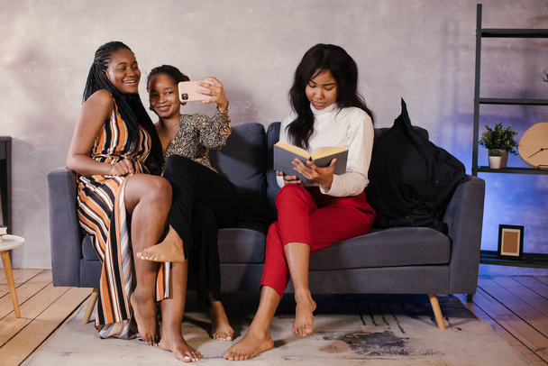 Τρεις Αφροαμερικανίδες κάθονται στον καναπέ και συζητούν κάτι. - Φωτογραφία, εικόνα
