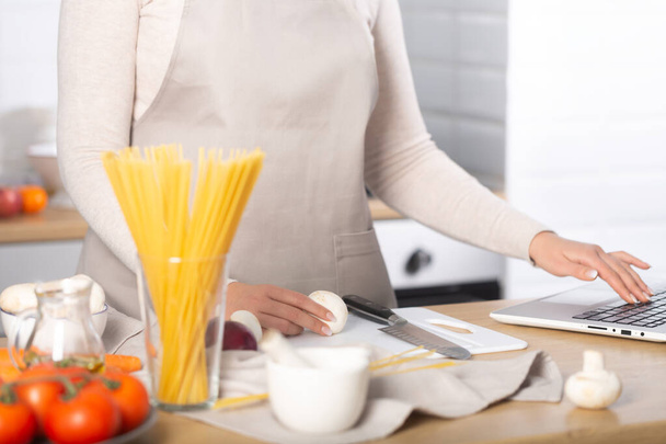 Woman cooking pasta using the computer to watch virtual culinary class - Fotó, kép