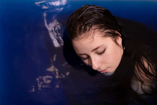 Porträt einer attraktiven brünetten Frau oben ohne in blauer Flüssigkeit. in Badewanne mit farbigem Wasser. Ertrinkendes Mädchen. Kopierraum - Foto, Bild