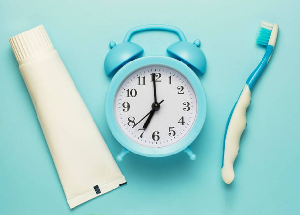 blue alarm clock with a tube of toothpaste and a baby toothbrush on a blue background. concept of cleaning and caring for teeth from an early age. copy space. flat lay - Photo, Image