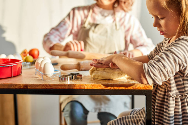 caring mommy helping cute smiling little preschool child daughter rolling dough for homemade cookies - 写真・画像