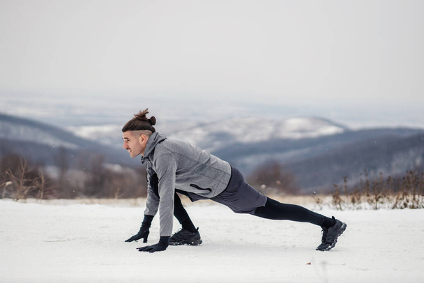 Fit sportsman in start position. Sportsman doing exercises on snowy weather in nature. Nature, outdoor fitness, winter fitness - Photo, Image