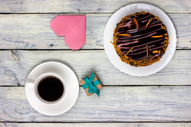 Chocolate cake, a cup of coffee, a heart shaped note and a small gift on a wooden table. Festive Flat Lay. - Foto, imagen