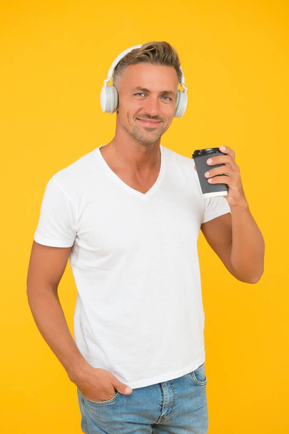 Caucasian middle-aged man drink takeaway coffee listening to music in casual fashion style yellow background, drinking - 写真・画像