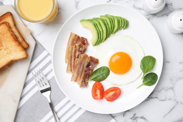 Tasty breakfast with fried egg, bacon and avocado served on white marble table, flat lay - Valokuva, kuva