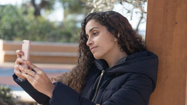 молодая девушка смотрит на смартфон и делает в парке - Фото, изображение
