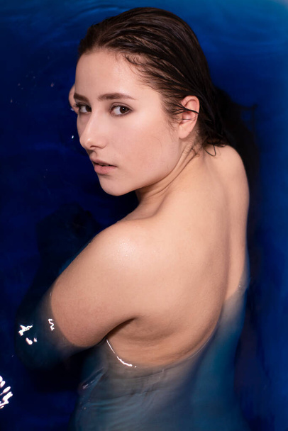 Mavi sıvı içinde üstsüz esmer bir kadının portresi. Renkli suyla dolu küvette. Boğulan kız. Boşluğu kopyala - Fotoğraf, Görsel