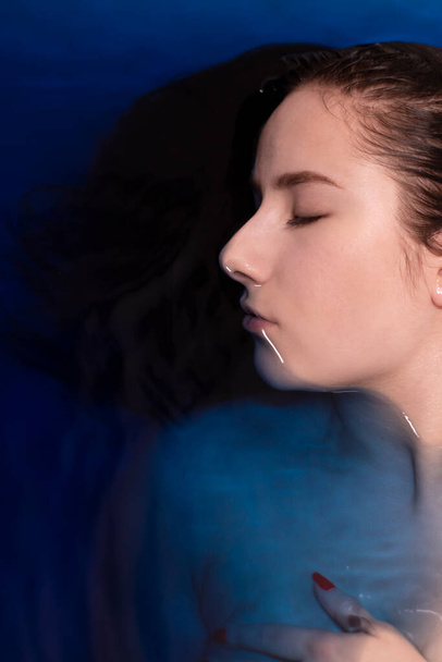 πορτρέτο της ελκυστική μελαχρινή γυναίκα τόπλες σε μπλε υγρό. σε μπανιέρα με χρωματιστό νερό. πνιγμό κορίτσι. αντίγραφο χώρου - Φωτογραφία, εικόνα