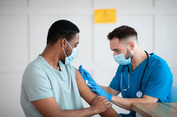Homme afro-américain masqué recevant un vaccin contre le coronavirus, prenant un vaccin covid-19 au cabinet médical - Photo, image