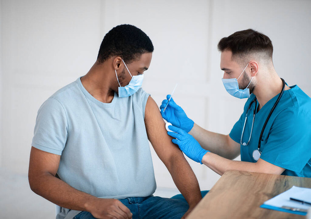 Ιατρός ή νοσοκόμος που χορηγεί εμβόλιο για τον ιό της στέψης σε αφροαμερικανό ασθενή στην κλινική - Φωτογραφία, εικόνα
