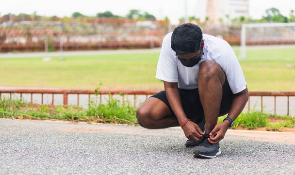 Азиатский спортивный бегун чернокожий мужчина носит часы сидя он пробует беговые кроссовки шнурки, готовясь к бегу и бегу в открытом уличном парке здоровья, концепция здорового упражнения тренировки - Фото, изображение