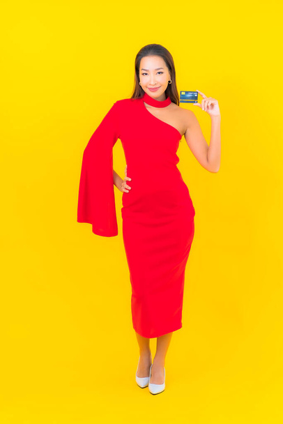 Retrato bonito jovem asiático mulher com cartão de crédito no fundo amarelo - Foto, Imagem