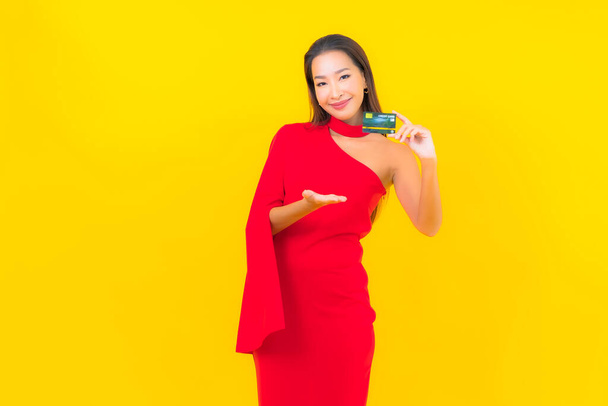Retrato hermosa joven asiática mujer con tarjeta de crédito sobre fondo amarillo - Foto, Imagen