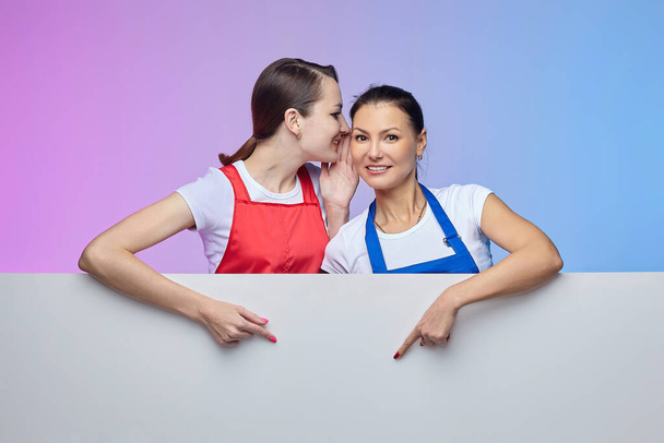 two girls in aprons pose with a white Billboard. advertising concept - Фото, зображення