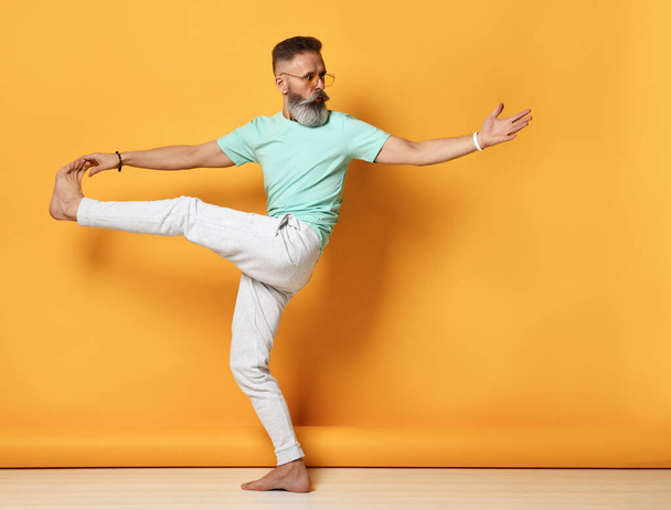 Stylish trendy gray-haired hipster guy dancing and having fun on bright orange background. - Фото, изображение
