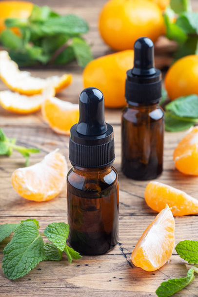Aromatic tangerine oil in a dark bubble, cosmetic oil from Mandarin on a wooden background, copy space - 写真・画像