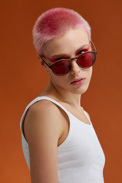 Nonconformist girl with pink short hairs with red sunglasses, over brown background. Vertical view. - Valokuva, kuva