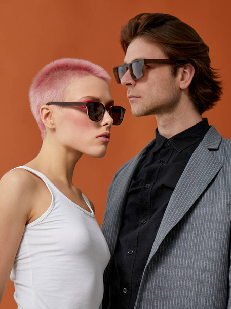 Portrait de profil d'un jeune couple hipster élégant en lunettes de soleil, posant ensemble sur un fond brun. - Photo, image