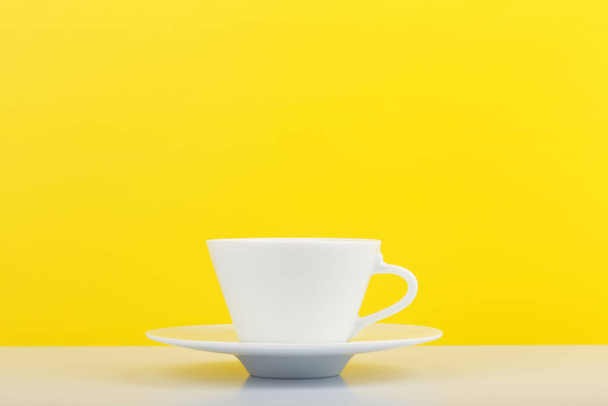 White glossy cup of coffee on white table against yellow background with copy space - Photo, Image