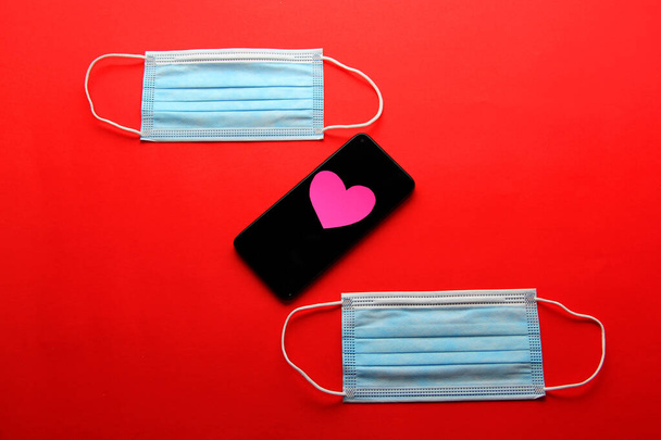 Valentýn u pandemie od covid-19, mobilní telefon s ochrannou maskou klinické použití a růžová srdce - Fotografie, Obrázek