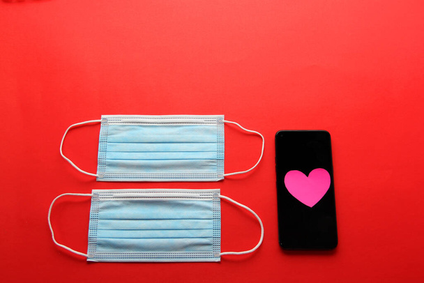 Walentynki w pandemii przez covid-19, telefon komórkowy z maską ochronną zastosowanie kliniczne i różowe serca - Zdjęcie, obraz