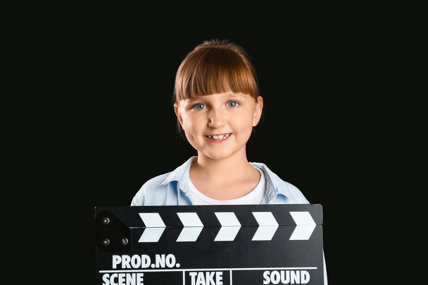 Kleines Mädchen mit Filmklöppel auf dunklem Hintergrund - Foto, Bild