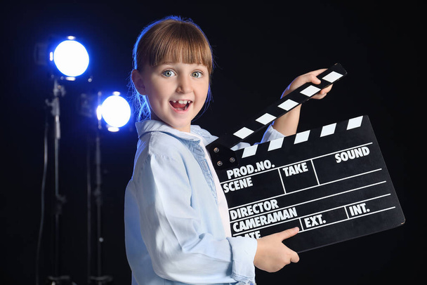 Klein meisje met film clapper op donkere achtergrond - Foto, afbeelding