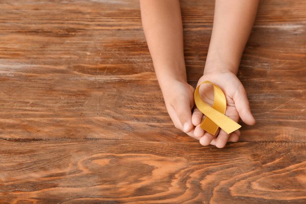 Child's hands with golden ribbon on wooden background. Cancer awareness concept - Foto, imagen