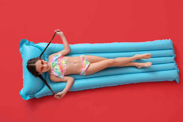 Cute little girl lying on inflatable mattress against color background - Foto, Imagen