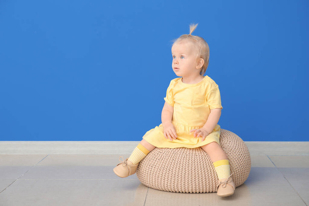 Портрет милой маленькой девочки, сидящей на пуфе возле цветной стены - Фото, изображение