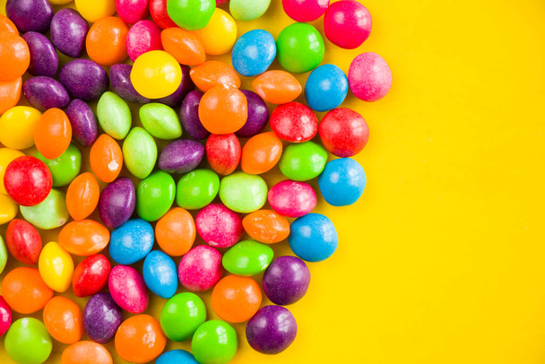 Skittles candy on the yellow table, colorful sweet candy background, high angle view - Foto, Imagem
