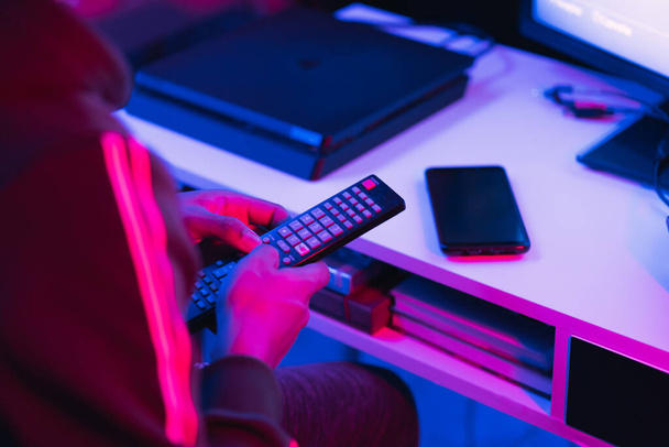 A high angle shot of a young male switching between channels with a remote control in a room with colorful lelights - Fotó, kép