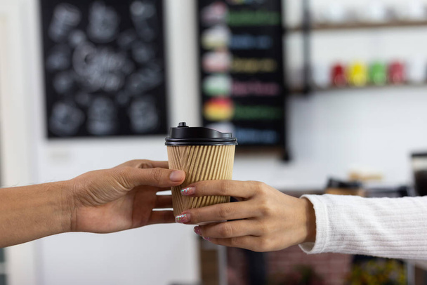 крупным планом бариста держит бумажные чашки кофе для клиента. - Фото, изображение
