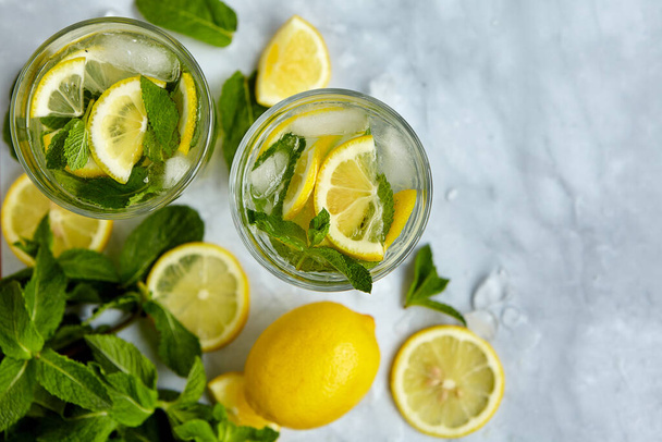 Osvěžující nápoje na léto, studená sladkokyselá limonádová šťáva ve sklenicích s nakrájenými čerstvými citrony. Osvěžující letní drink. Tradiční limonáda s citrónem, mátou a ledem. Selektivní zaměření - Fotografie, Obrázek