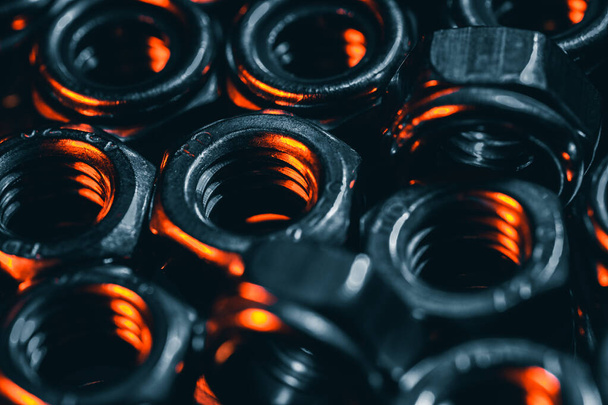 Een close-up shot van kleine metalen schroefmoeren in een donkere atmosfeer met oranje lampjes erop - Foto, afbeelding