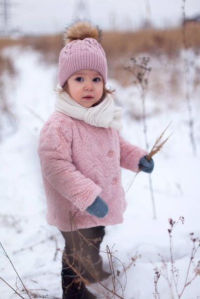 A little girl in a pink fur coat is having fun, playing outside, surrounded by snow. Winter time, the concept of healthy children's activity - Foto, afbeelding