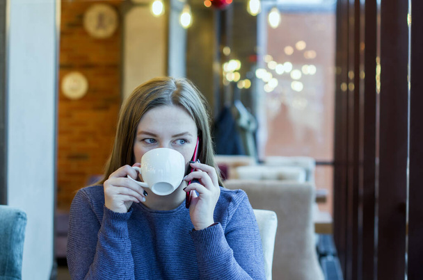 Young woman freelancer enjoying coffee during cellular conversation in cafe interior, having talking conversation with mobile phone while rest in cafe - Photo, Image