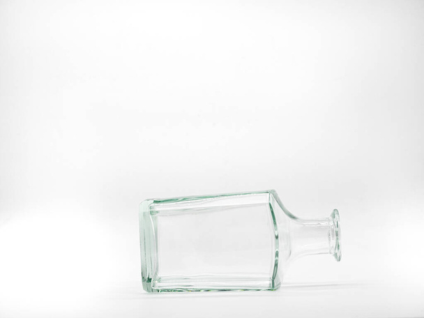 Single empty glass bottle on a white background. Transparent square bottle. Front view of the laying on its side transparent square bottle. - Photo, Image