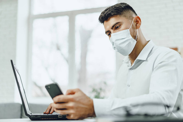 Young businessman sitting at his working desk with medical mask on - Foto, imagen